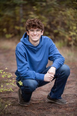 Person in blue sweatshirt crouches outdoors in autumn setting with blurred natural background.
