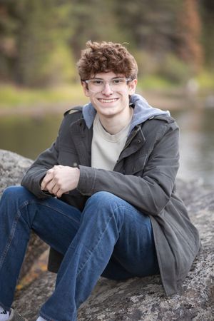 Portrait series of a person in a gray jacket and jeans sitting on rocks by a lake in natural outdoor lighting.