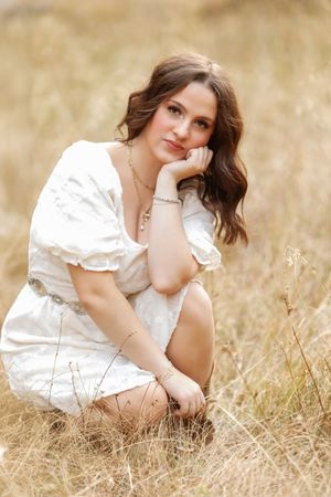 A dreamy outdoor portrait series showing someone in a white dress reclining in golden grass during sunset.