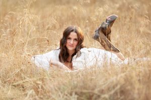 A person in a white dress lies in a golden field of tall grass during a dreamy outdoor photo session.