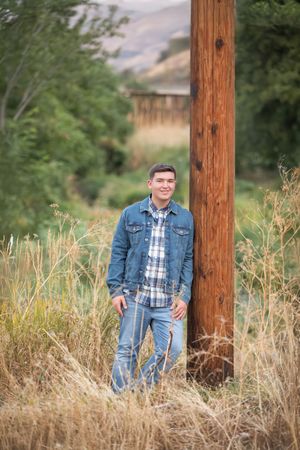 A senior portrait session in a rustic outdoor setting with wooden posts and tall dried grass.