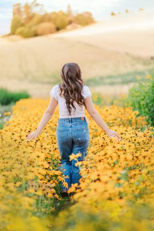A field of vibrant yellow wildflowers with someone in jeans walking through them during golden hour.