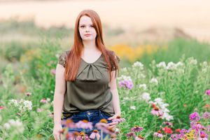Person in olive top sitting among colorful wildflowers in a summer meadow.