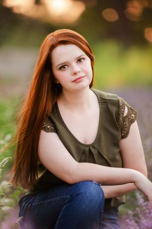 Portrait in an olive green top with long hair against a blurred nature background.