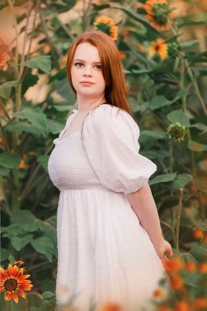 Person in a white dress with puff sleeves standing among blooming sunflowers.