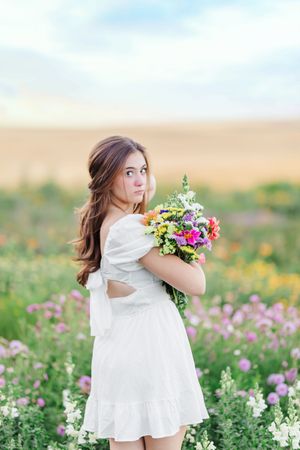 A whimsical scene in a wildflower meadow with someone in a flowing white dress holding a bouquet.