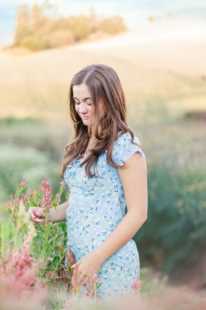 A dreamy summer scene with someone in a blue floral dress touching pink wildflowers.