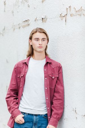 A casual portrait featuring a burgundy denim jacket and white t-shirt against a textured wall.
