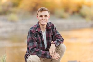 Person in plaid shirt poses outdoors during golden hour with mountains in background.