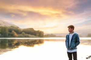 Scenic lakeside landscape at sunset with golden clouds reflecting on calm water.