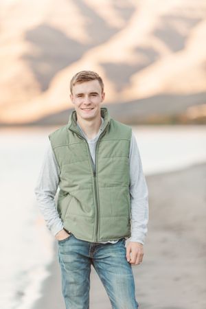 Person wearing a green vest and light colored shirt poses outdoors against a blurred natural background.