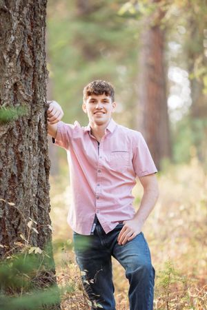 Outdoor portraits between pine trees showing someone in a pink shirt posing casually.