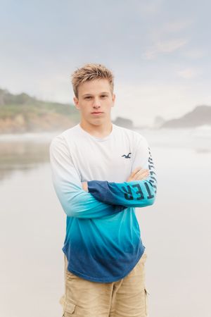 Person in ombre blue and white long sleeve shirt standing on misty beach.
