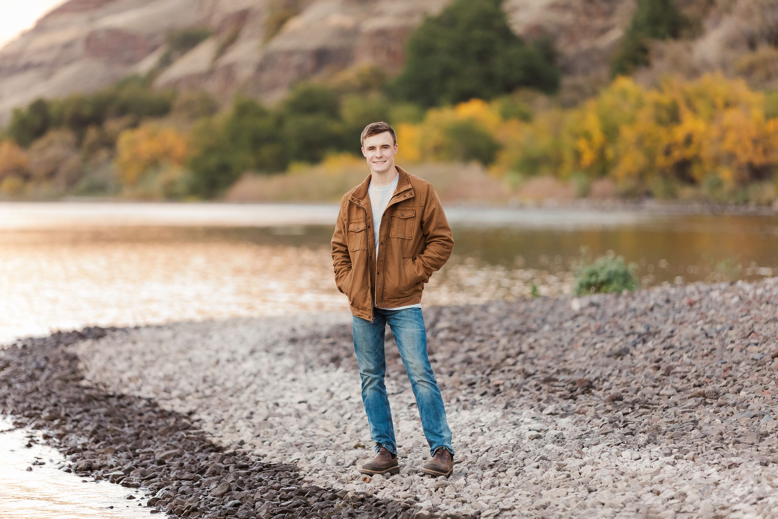 Rocky shoreline with mountains and autumn foliage in background during sunset.