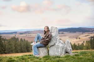 Person relaxing on a large boulder while enjoying scenic mountain views and rolling hills in the countryside.