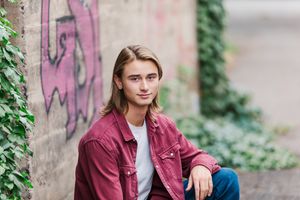 A casual portrait against a weathered wall with graffiti and climbing vines.