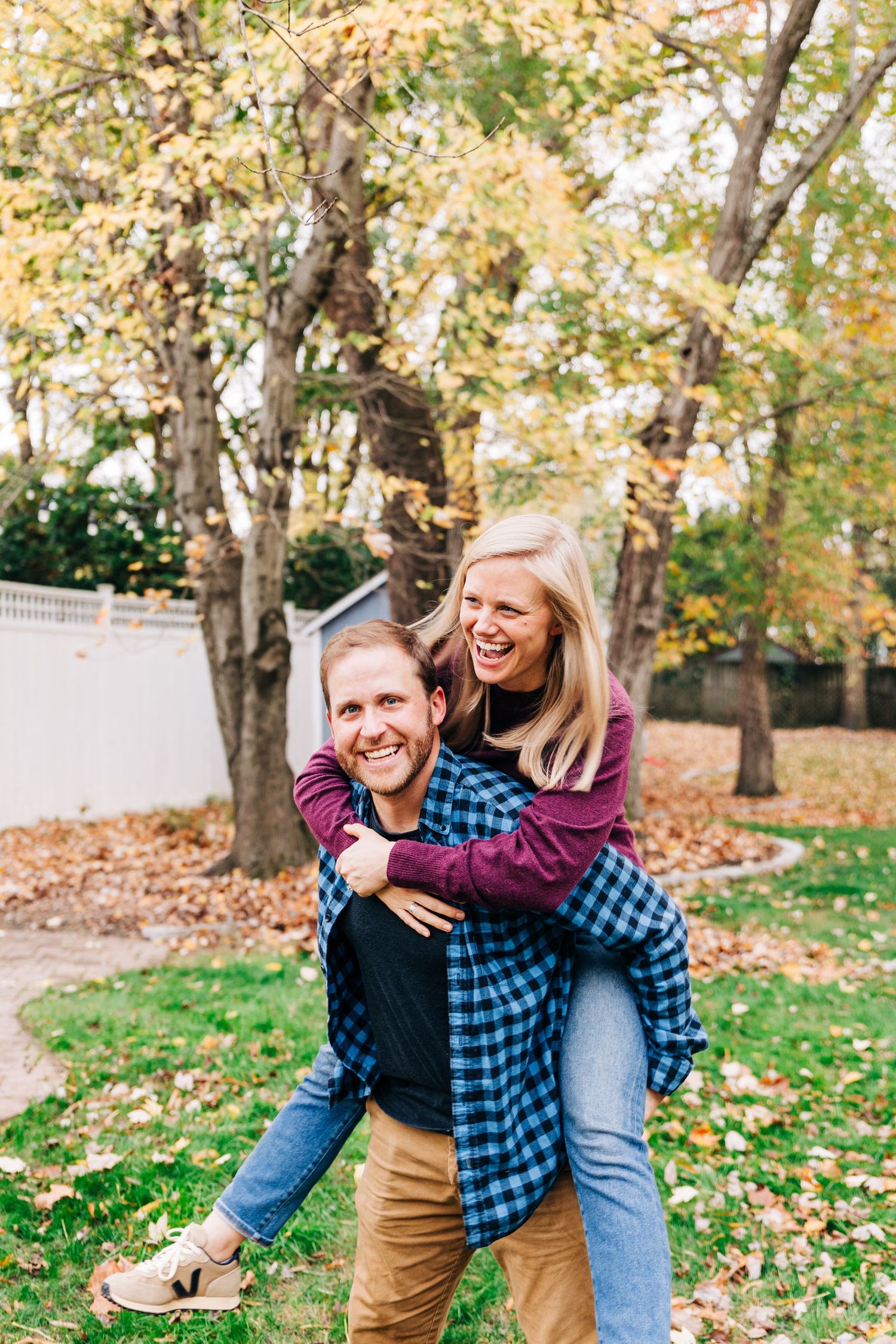 Playful couple enjoys fall weather in their Charlotte backyard with autumn leaves scattered on the grass.