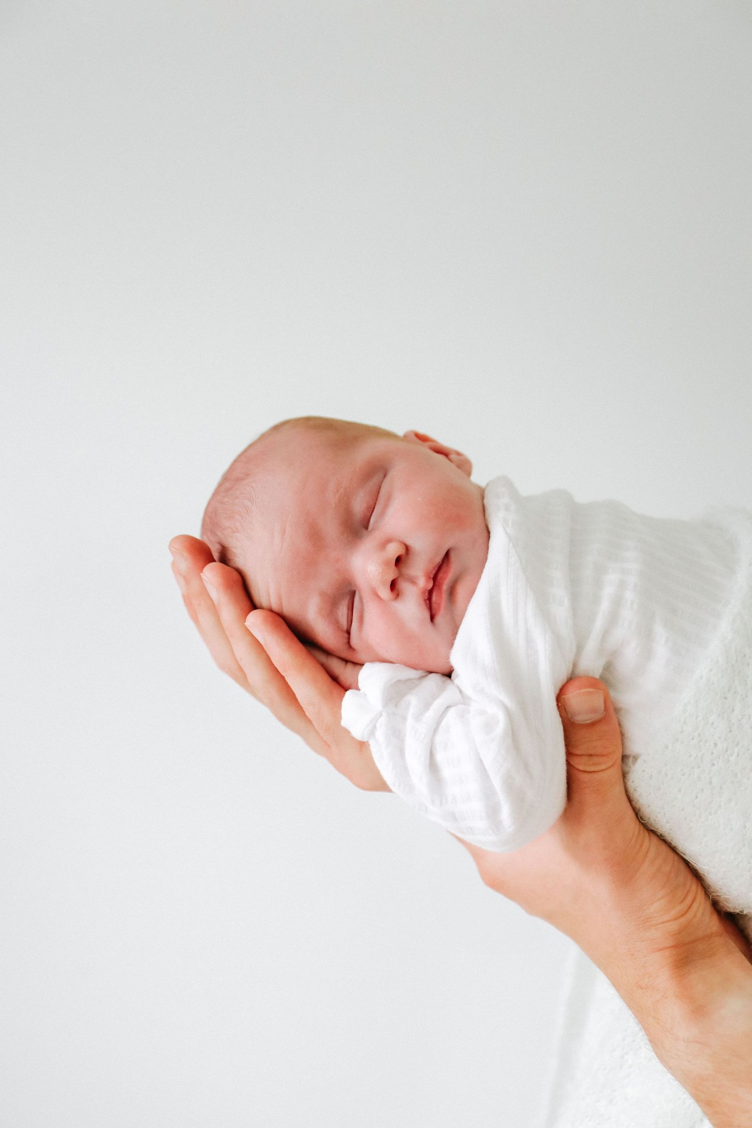 A tiny newborn baby is gently cradled in an adult's hands against a light background, during newborn shoot based in Nottingham