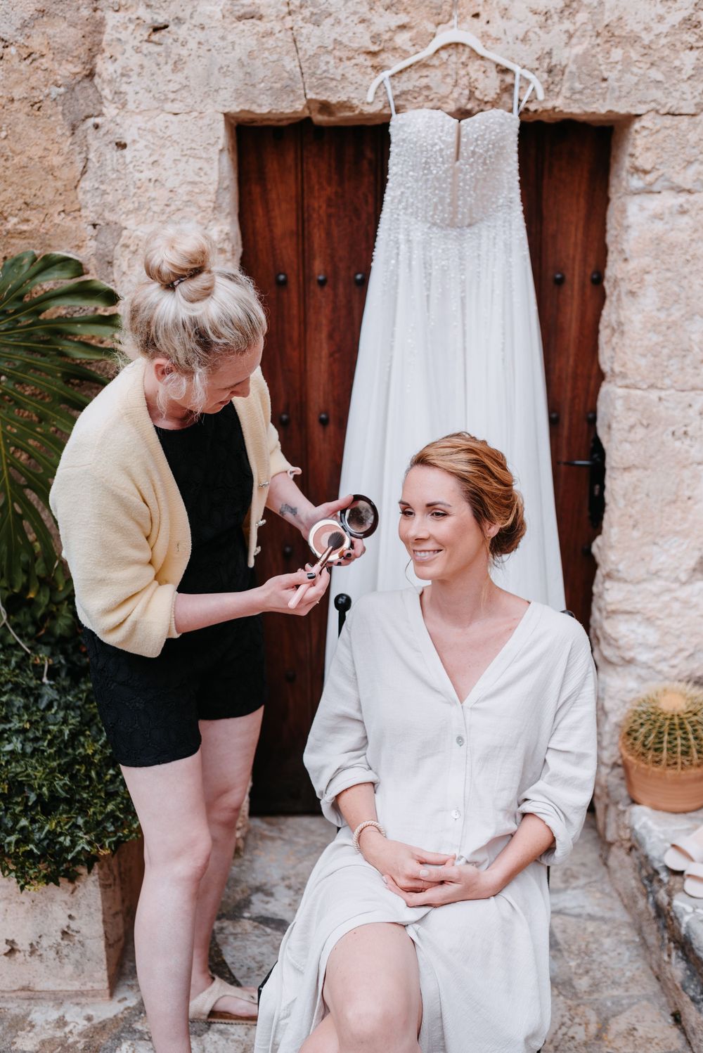 Hochzeitsvorbereitungen: Ein weißes Brautkleid hängt an rustikalen Holztüren, darunter findet das Getting Ready auf Mallorca statt.