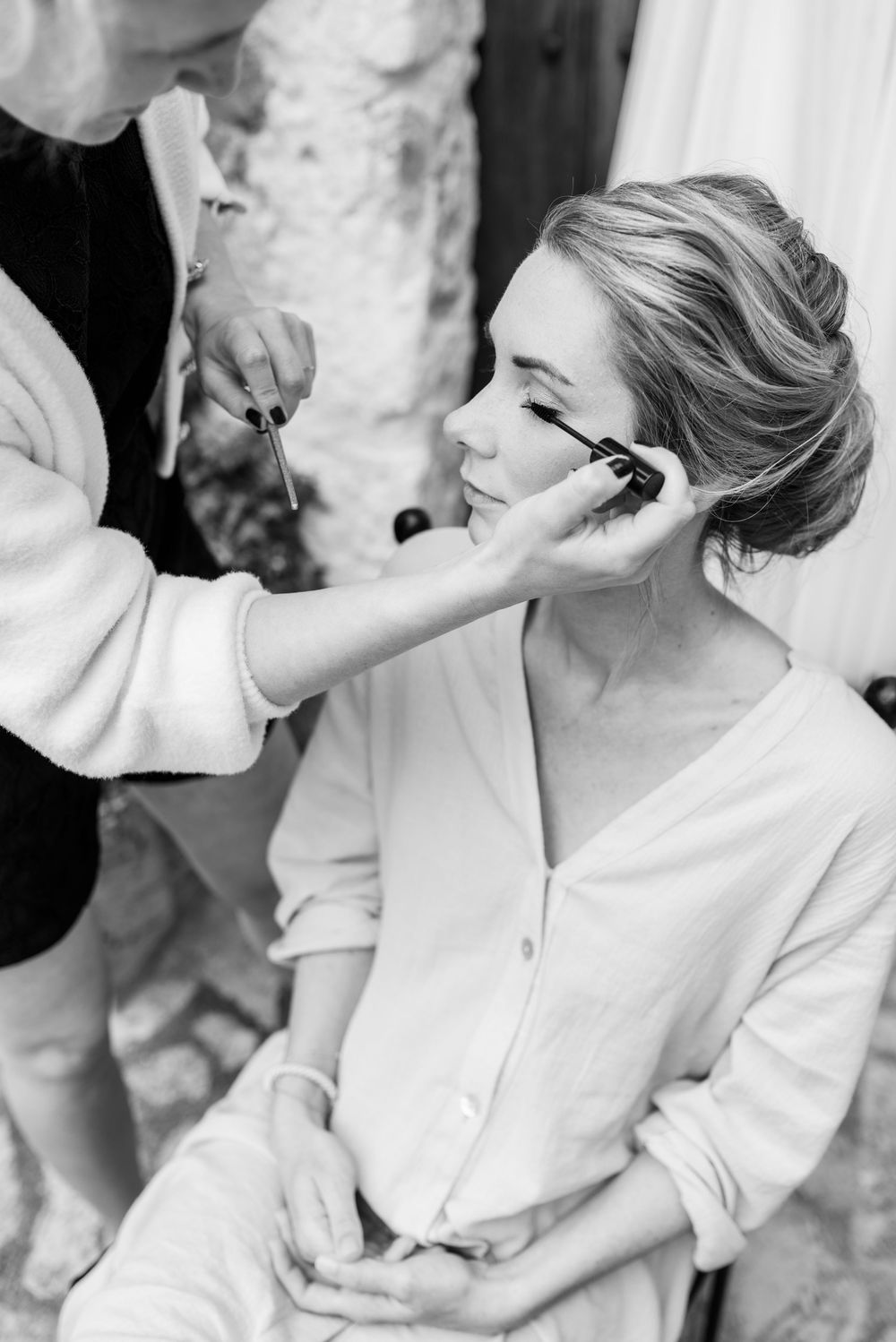 Schwarz-Weiß-Foto einer Visagistin, die einer Frau, die sich für die Hochzeitsvorbereitungen fertig macht, Mascara aufträgt. Finca Xiclati.