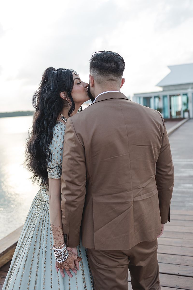 A couple shares an intimate moment on a wooden boardwalk by the water.