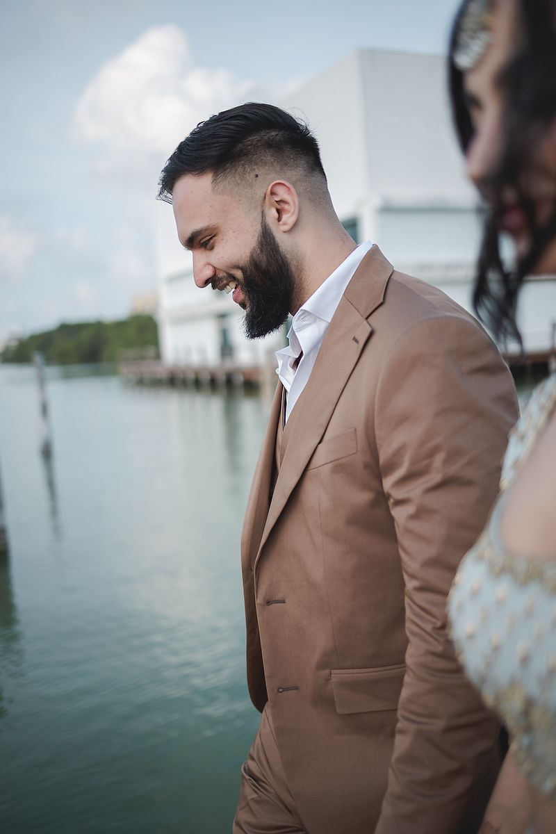 Formal-dressed person in brown suit smiling on waterfront dock.