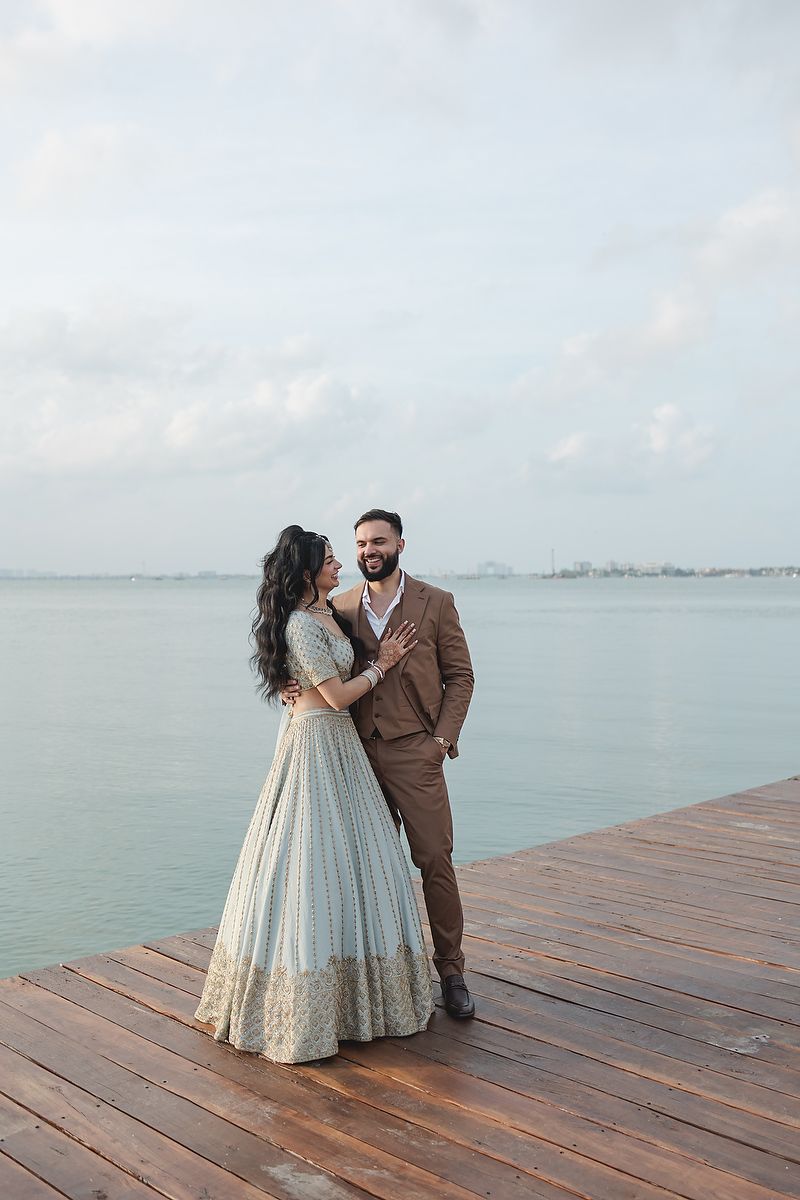 A romantic couple in formal wear poses on a waterfront wooden deck.