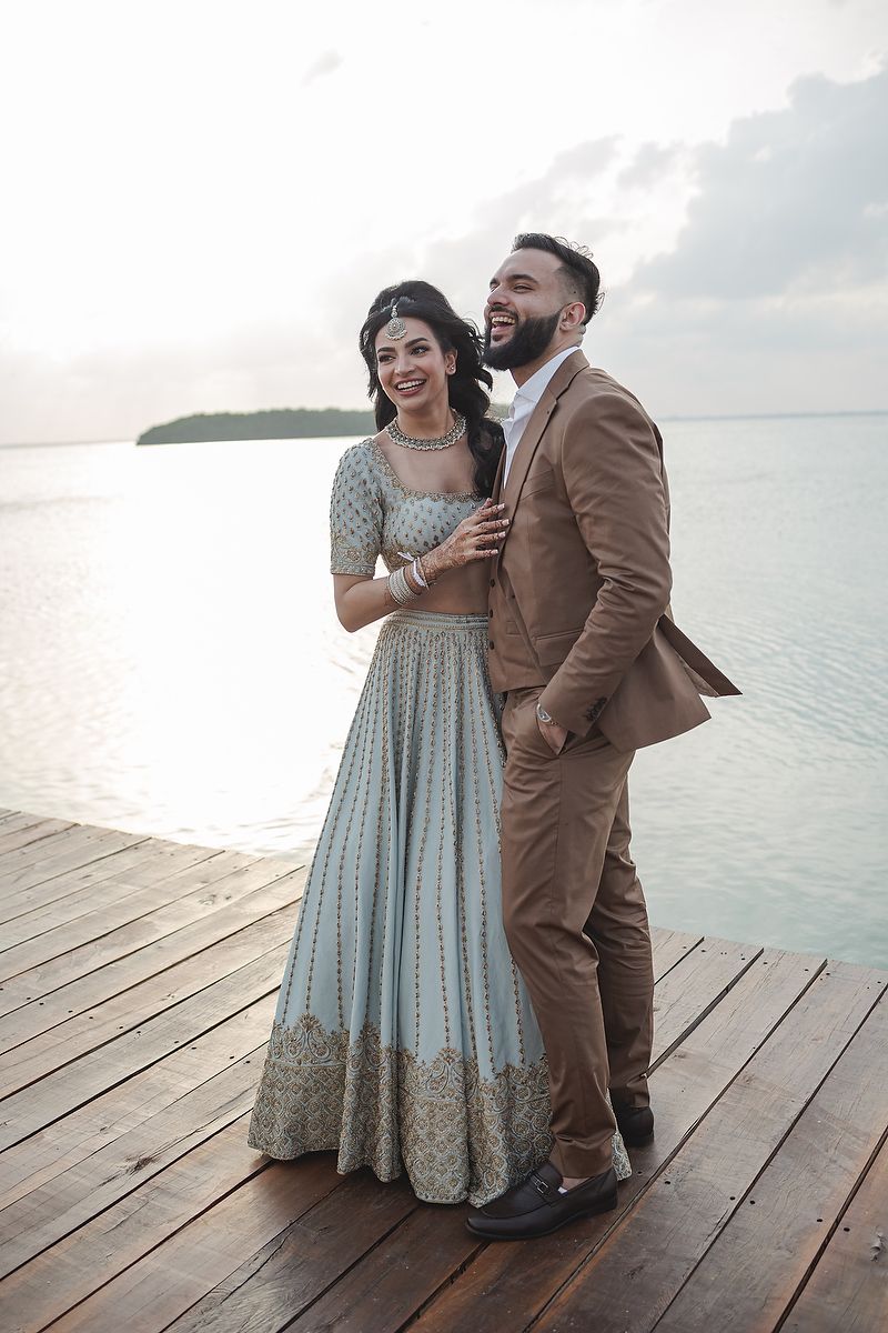 Couple in formal attire share a joyful moment on wooden dock by the water.
