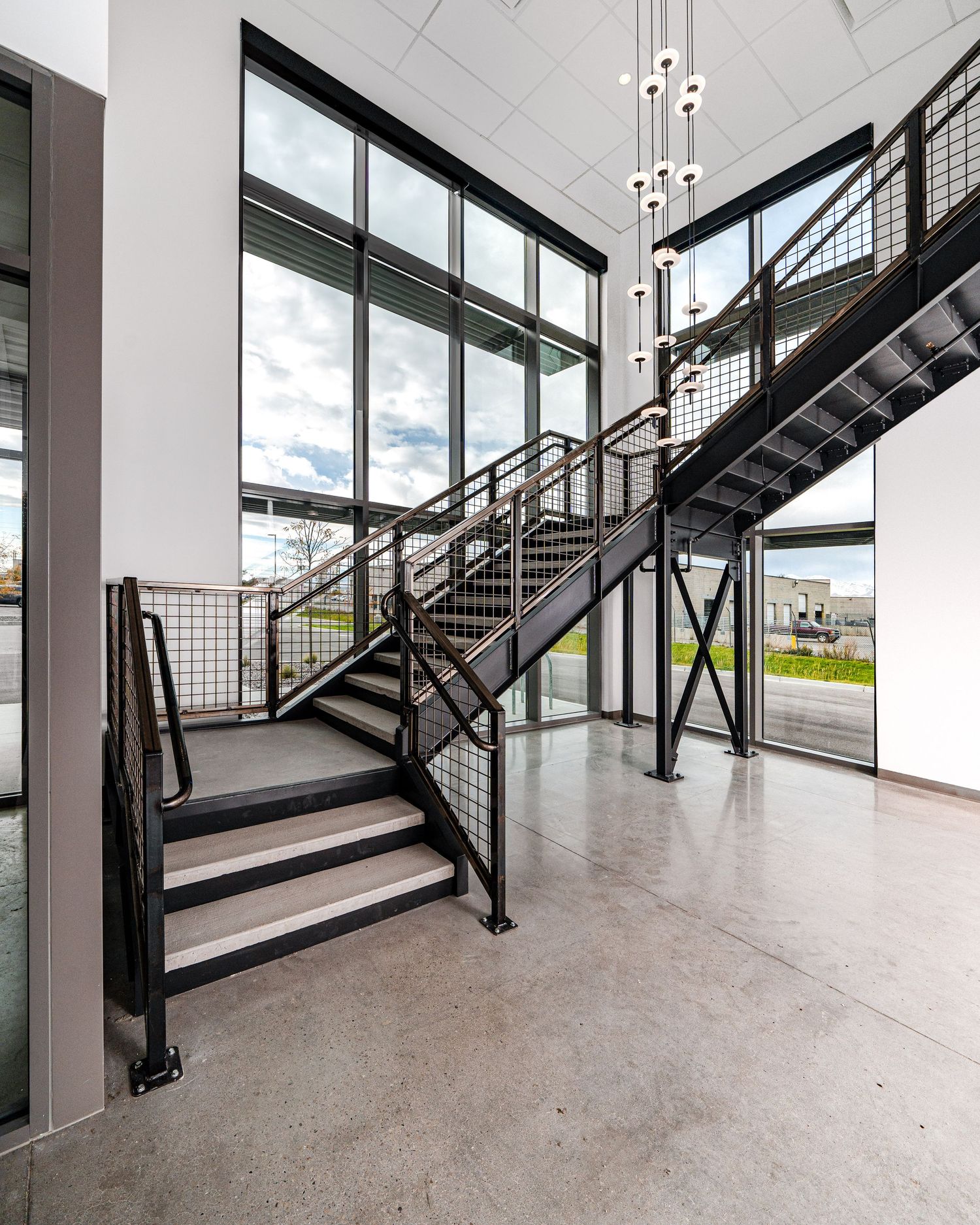 Modern industrial staircase with metal railings and large windows in contemporary building interior.