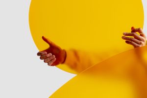 Human hands gesturing against a vibrant yellow curved background wall.