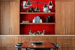 Modern kitchen with built-in wooden cabinets, red accent wall shelving unit, pendant lights and dining table.