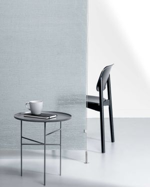 Minimalist interior scene with a round side table and modern black chair against a light gray wall.