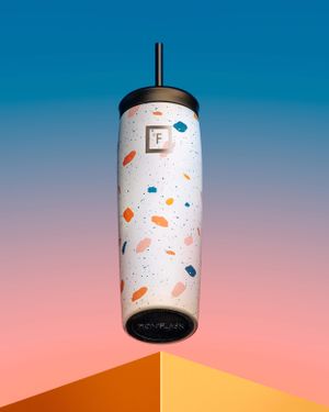 White terrazzo patterned tumbler with black lid against gradient blue and pink background.