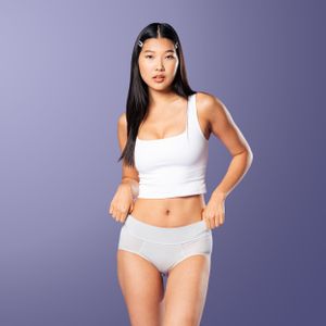 Athletic model in white crop top and underwear poses against purple background.