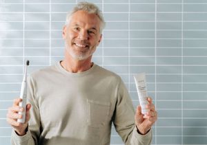 Person holding dental hygiene products while wearing a gray t-shirt.