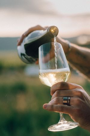 White wine being poured into a wine glass held against a blurred outdoor landscape background at sunset.