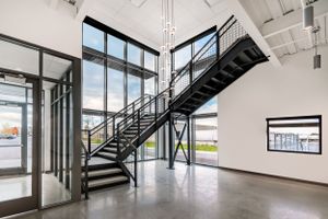 Modern industrial office interior featuring a floating metal staircase and glass walls.