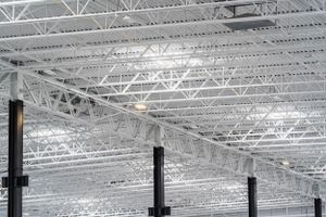 Industrial warehouse ceiling with exposed metal trusses and white steel framework.