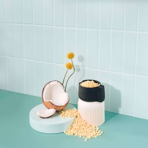 Split coconut with yellow crysanthemums and scattered grains displayed on turquoise and white background.