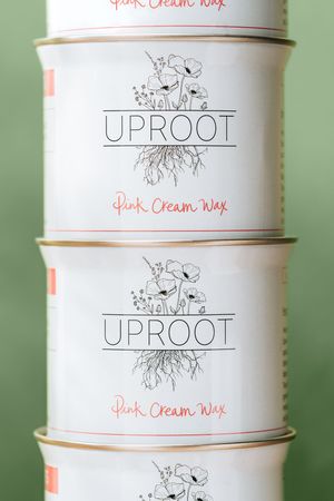 Stack of white cylindrical containers with Uproot Pink Cream Wax branding featuring delicate floral illustrations.