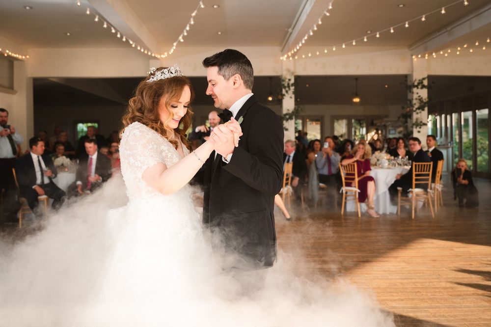 A couple shares their first dance on a misty dance floor with string lights overhead at an elegant wedding reception at The Garrison.