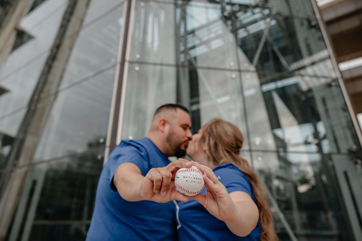Couple sharing intimate moments at a modern glass covered bridge or walkway, photographed in multiple candid poses.