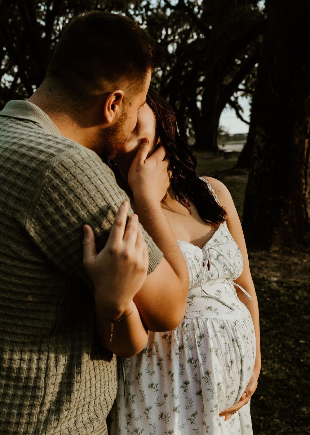 A tender embrace between a couple during a maternity photoshoot in a wooded setting.