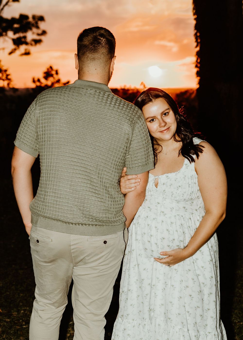 Expectant couple poses against a vibrant sunset backdrop.