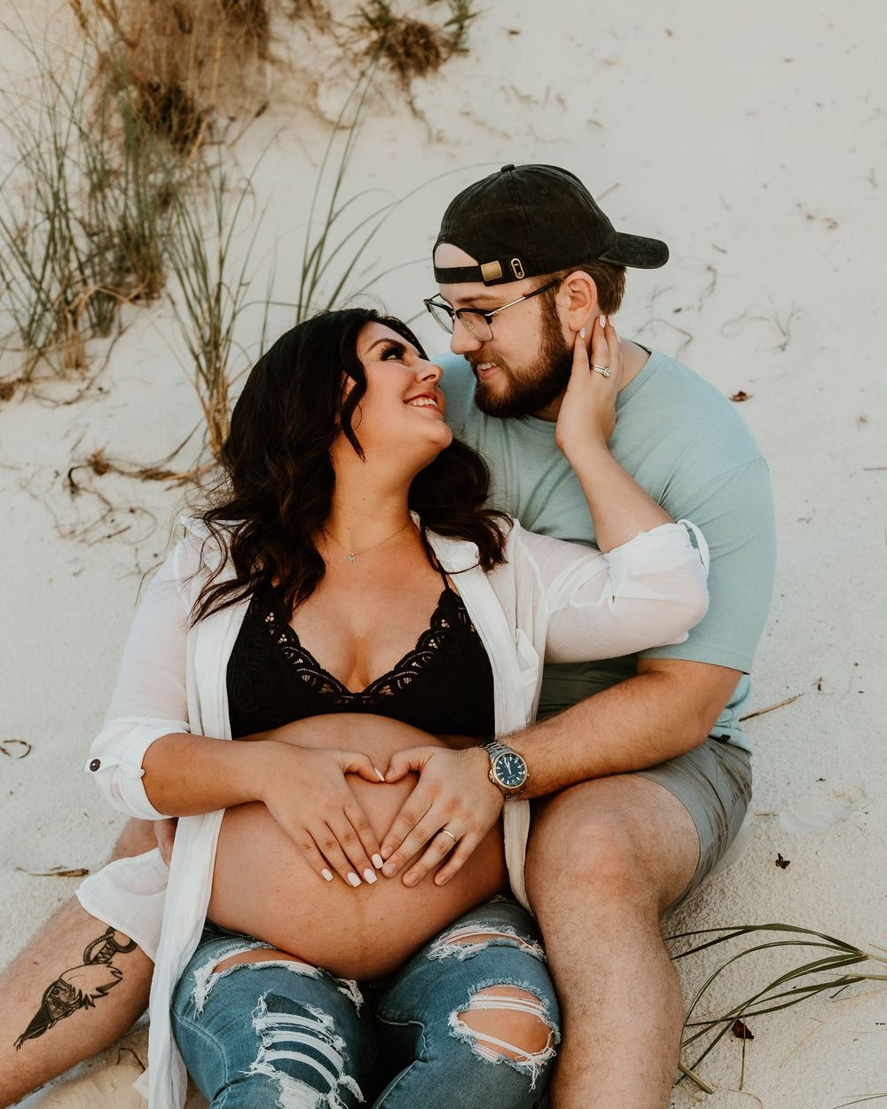 A couple lies on sand during an intimate beach photoshoot.