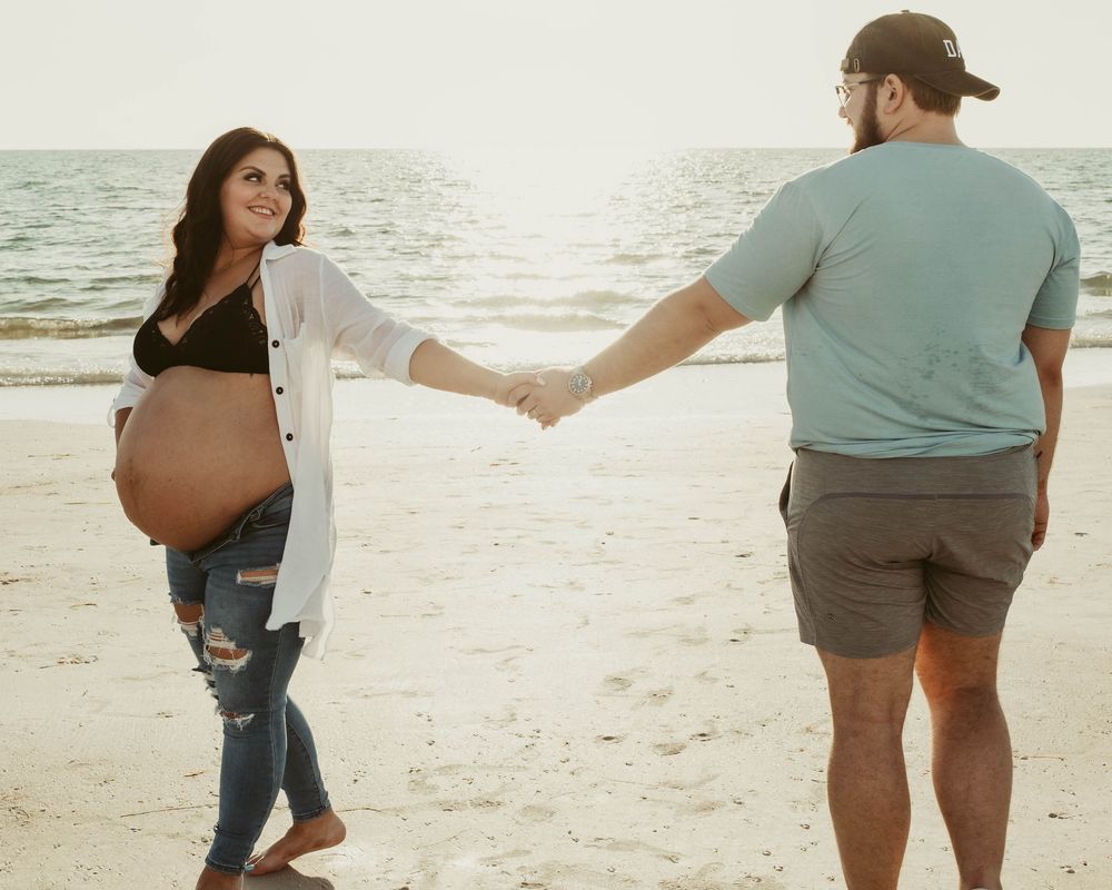 A couple walks together on a sandy beach at sunset holding hands and enjoying a tender moment.