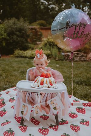 A strawberry-themed smash cake setup outdoors with pink decorations and balloons for a first birthday celebration.