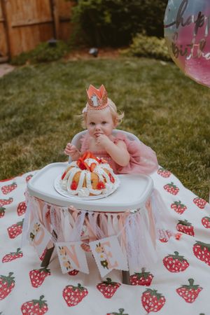 Pink and white decorated cake smash setup with strawberry print tablecloth and tulle details for first birthday celebration.
