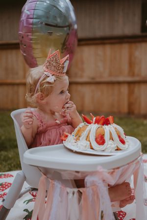 A child wearing a pink bow enjoying a decorated vanilla bundt cake with strawberries and whipped cream topping.