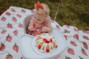 A strawberry-themed outdoor party setting with a pink frosted bundt cake and matching strawberry print blanket on grass.